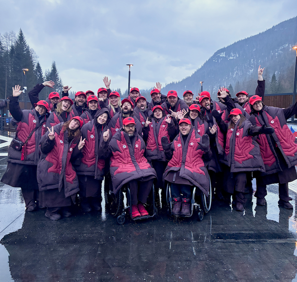 Canadian athletes gathered for a photo in red Paralympic apparel in front of a mountain background with a grey sky