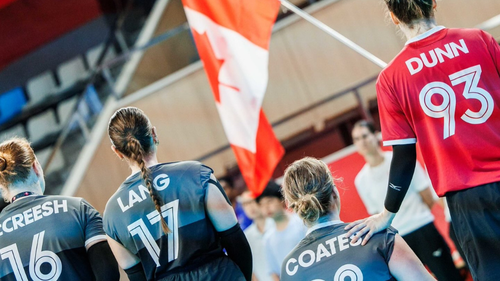 Canadian sitting volleyball players Ecreesh (16), Lang (17), and Coates stand together facing a Canadian flag, with a Team Canada player wearing "Dunn 93" beside them in the arena.