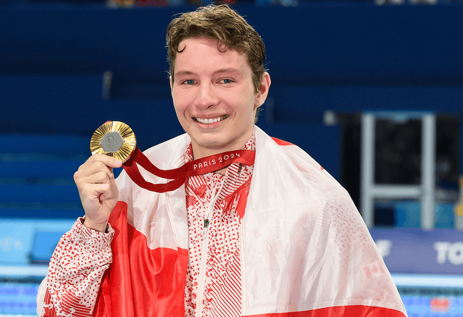 Nick Bennet, swimmer, posting with a flag around his shoulder and holding a medal